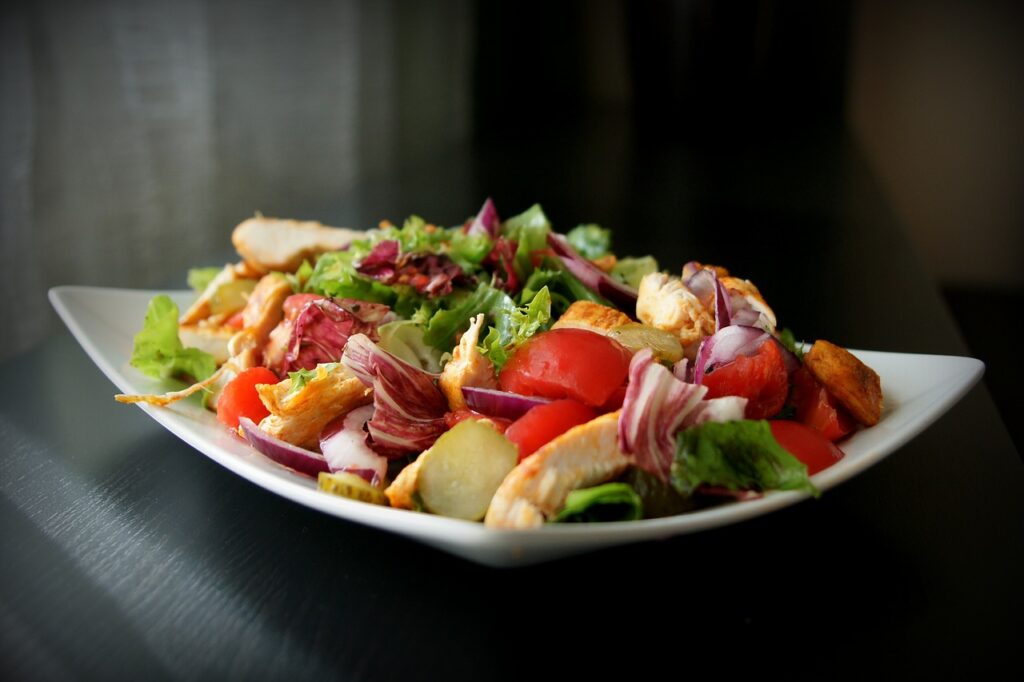 Une assiette de salade équilibrée avec du poulet grillé, des légumes frais comme des tomates et des radis, et une variété de feuilles vertes.