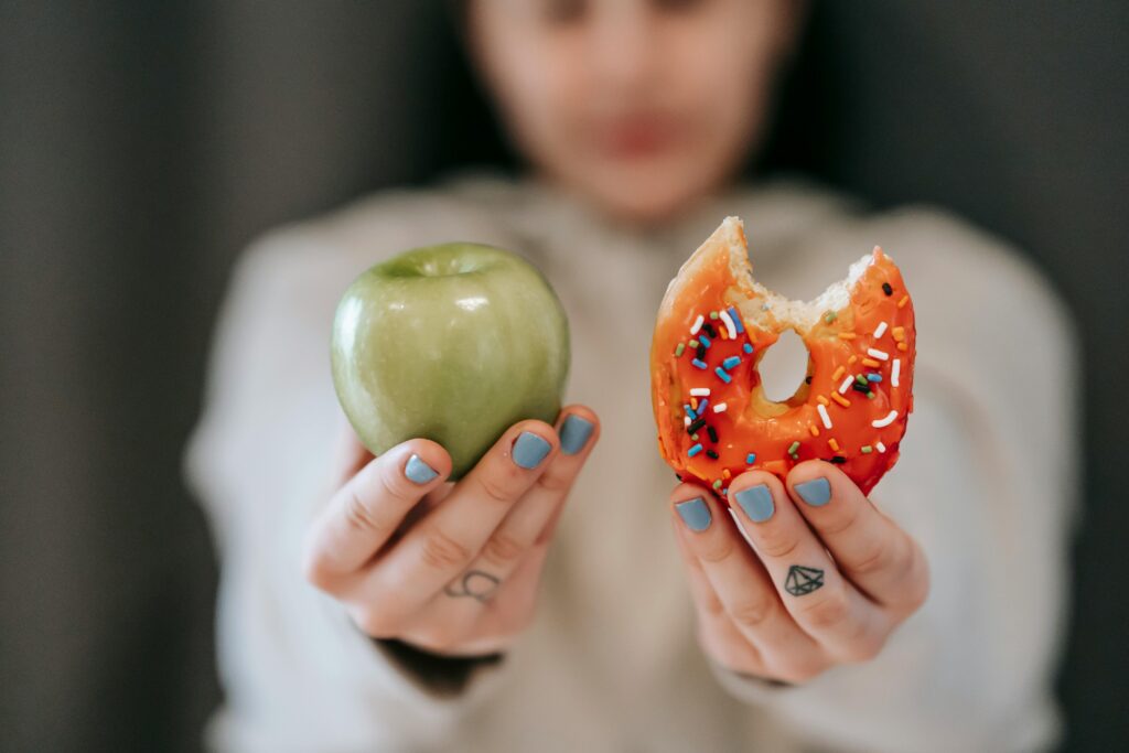 Personne tenant une pomme dans une main et un beignet dans l'autre, représentant le dilemme entre faim physique et émotionnelle.