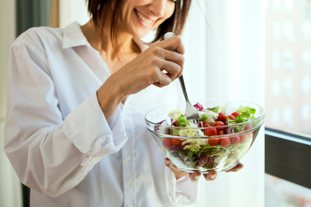 Femme souriante mangeant une salade, un exemple de manger en pleine conscience.